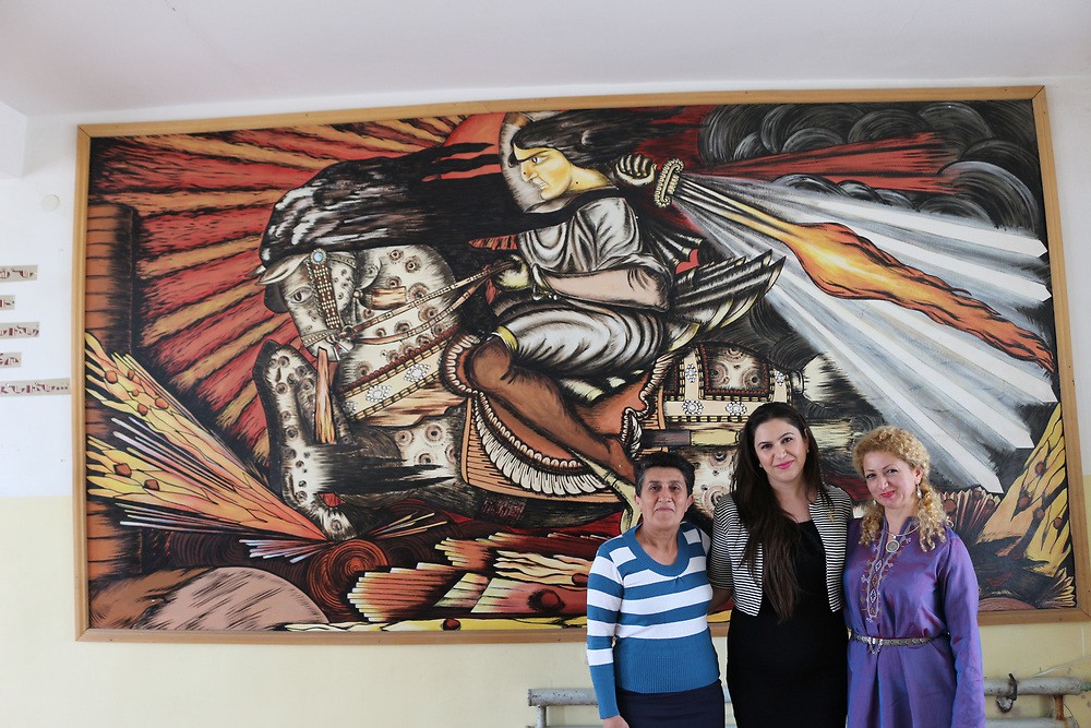 Teachers of Sasunik village stand in front of a mural of the Daredevils of Sassoun.